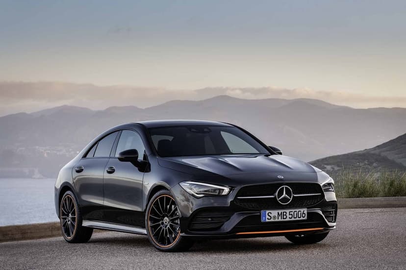 Black Mercedes-Benz CLA sedan with orange rim accents parked on a scenic coastal mountain road during sunset.