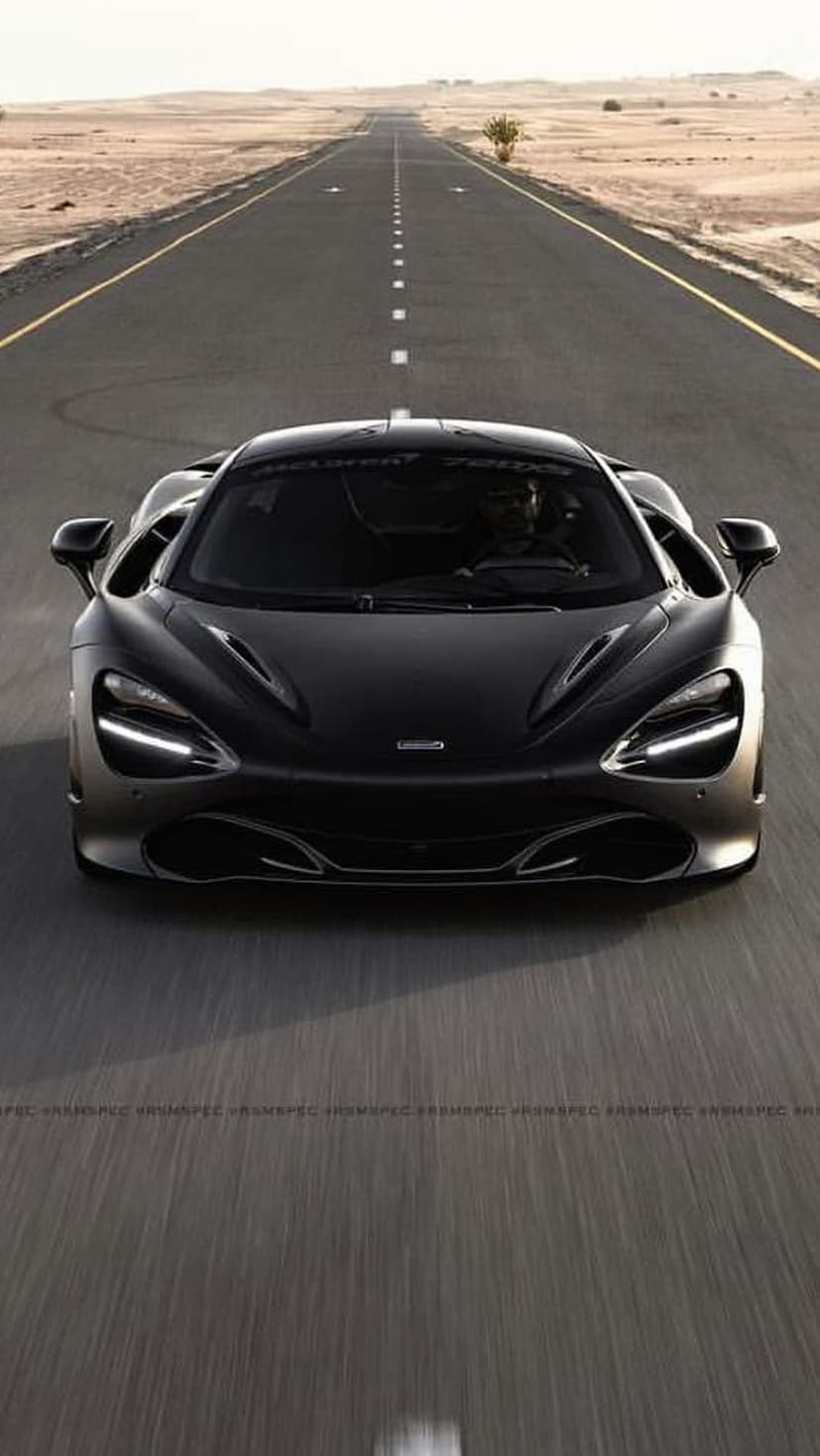 Black McLaren 720S supercar speeds along an empty desert highway under clear skies at a low perspective.