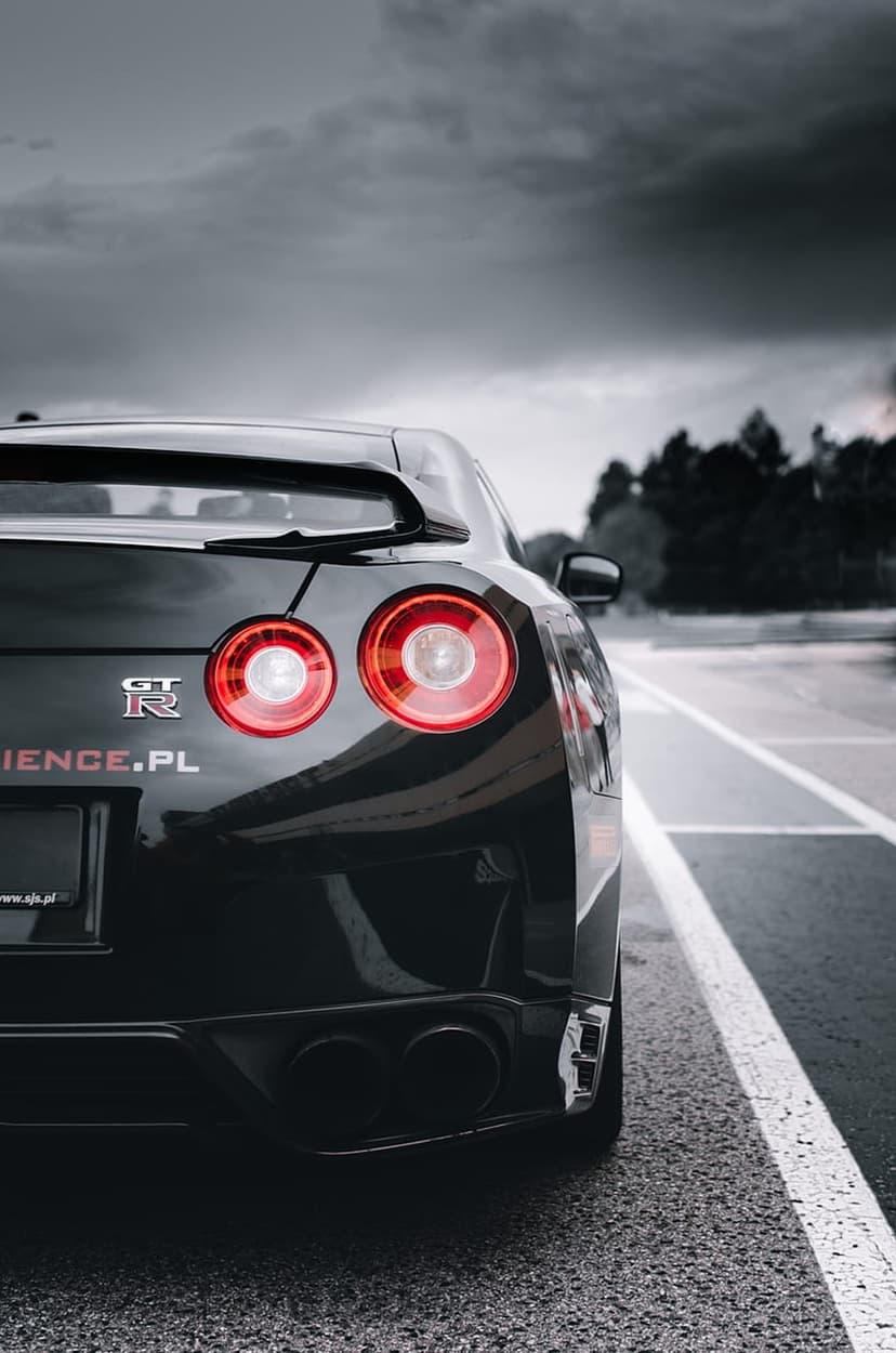 Black Nissan GT-R rear view with glowing red circular taillights on a road under a dark overcast sky.