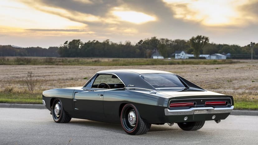 Dark green 1969 Dodge Charger muscle car parked on an open road at sunset with a vast rural field in the background.