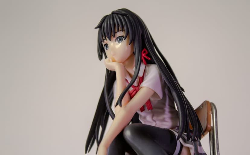Anime girl figurine in a school uniform sits with her hand on her chin, featuring black hair and a red ribbon.