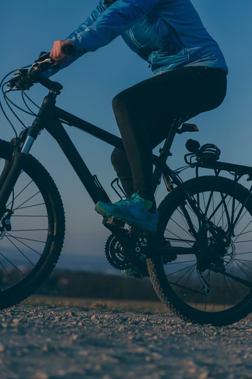 Cyclist in a blue jacket and black leggings rides a mountain bike on a sunny gravel path under a clear blue sky.
