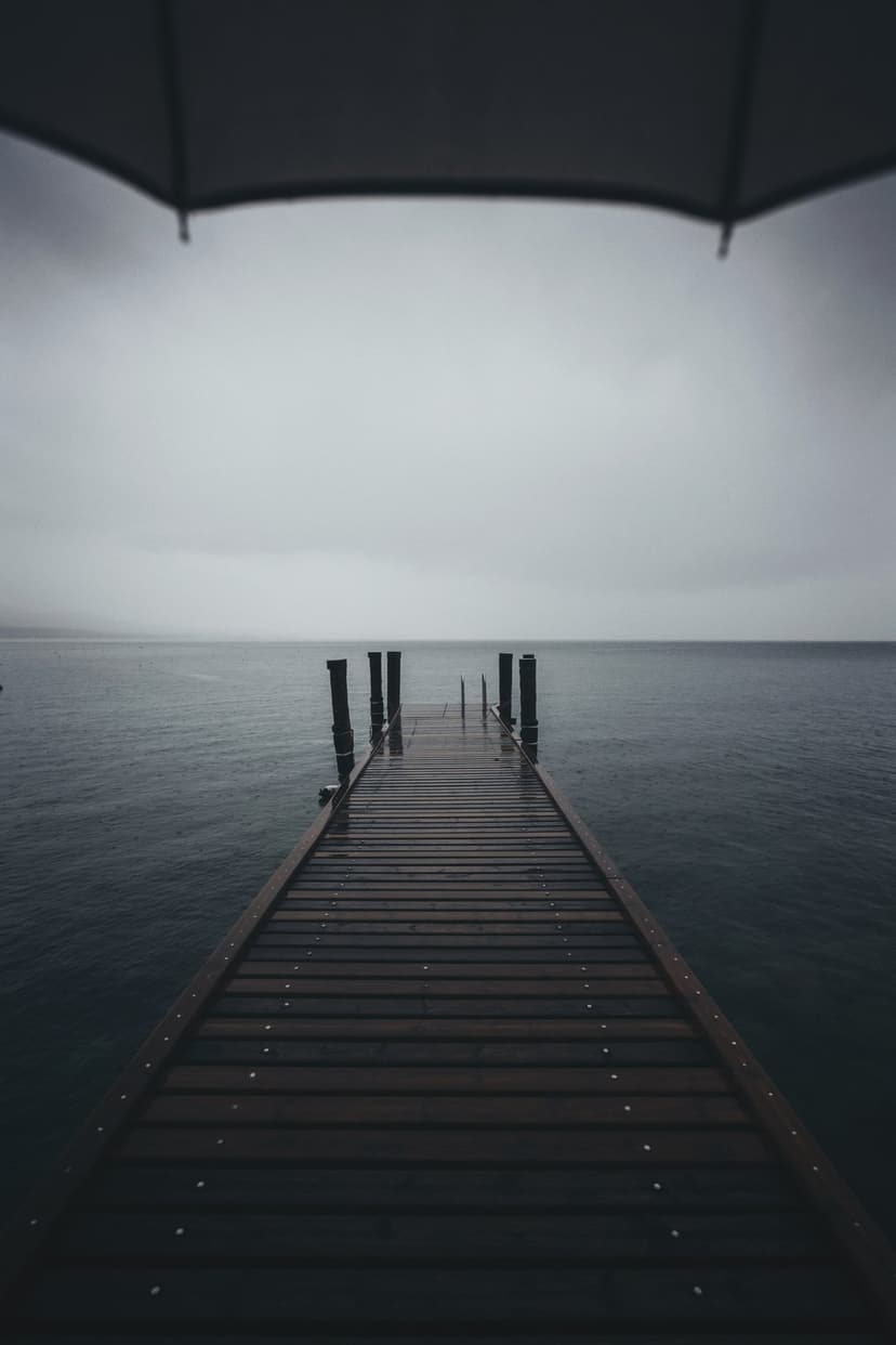 Weathered wooden pier leading into a vast misty lake under a heavy overcast sky with gray water and thick fog.