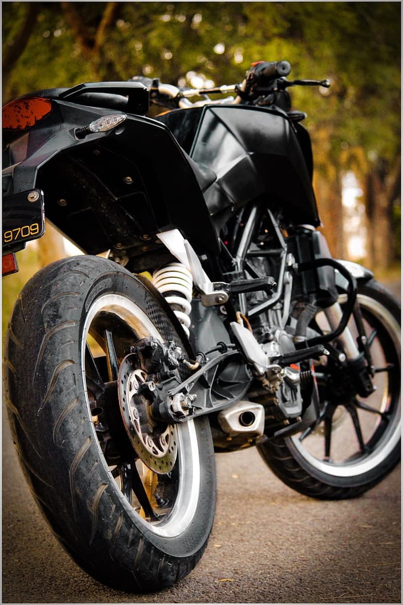 KTM Duke motorcycle rear wheel with white coilover shock absorber and disc brake on an outdoor road.