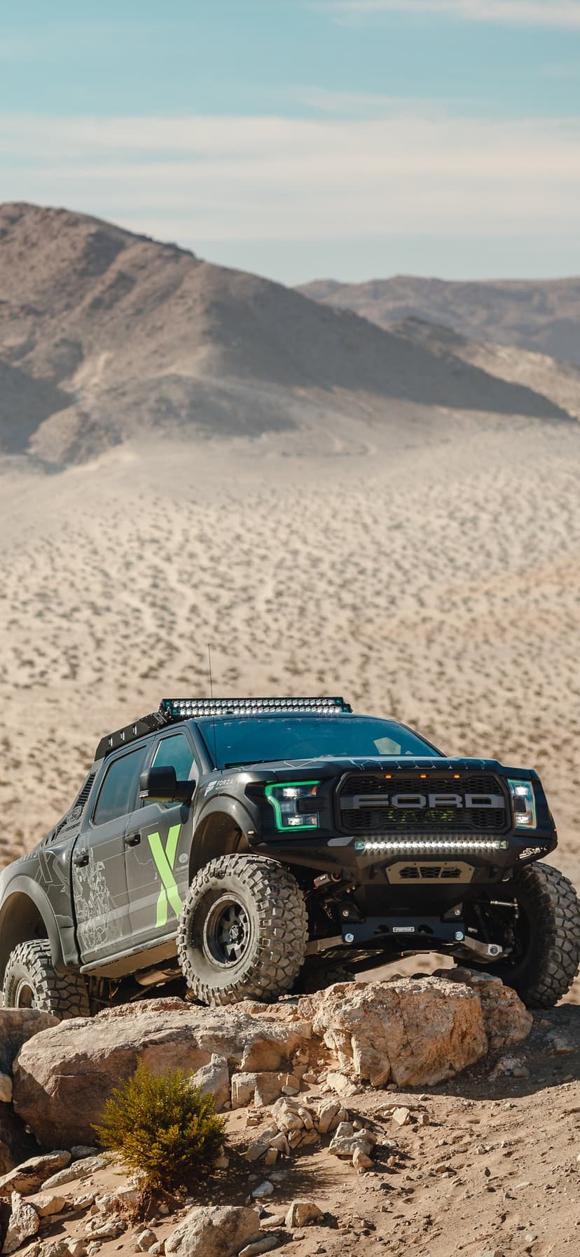 Custom Ford Raptor truck with lime green accents parked on desert rocks under a hazy sky.