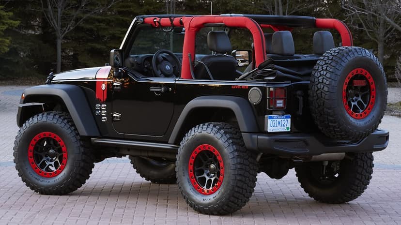 Black Jeep Wrangler with red roll bars and matching wheel rings parked on a paved lot with forest backdrop.
