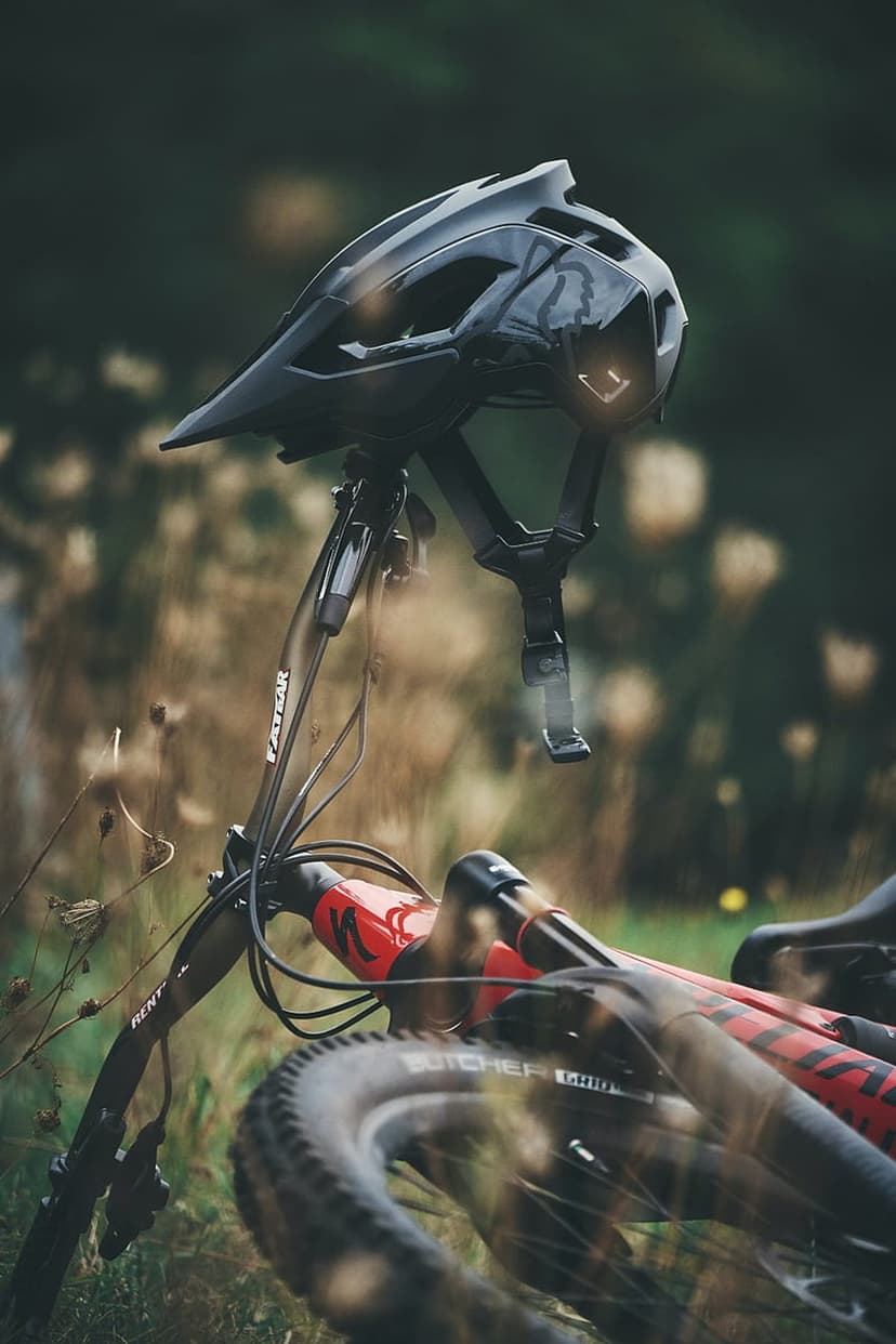 Black MTB helmet on bicycle handlebars amidst lush green grass and soft outdoor lighting on a trail.