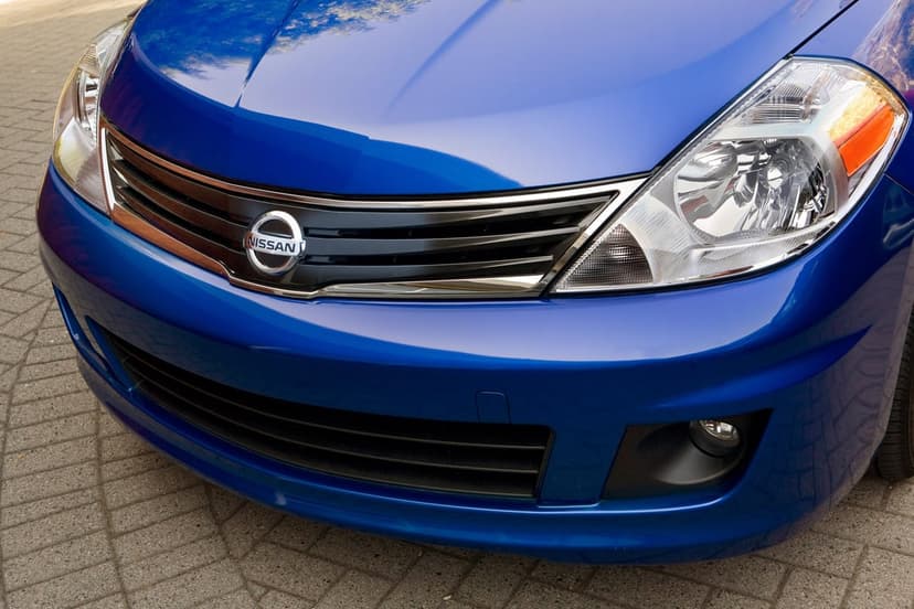 Blue Nissan front grille with silver logo, large clear headlight, and sleek metallic hood on brick paving.