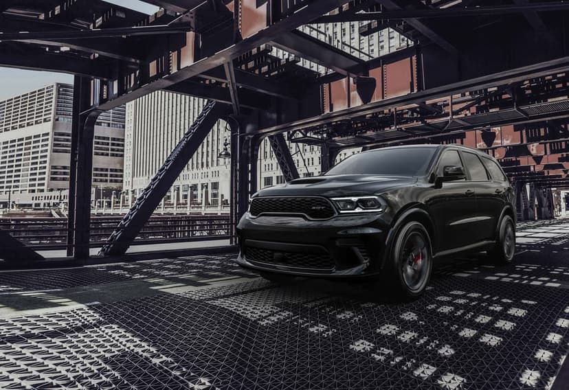 Black Dodge Durango SRT parked on a metal bridge deck framed by steel beams with a city skyline background.
