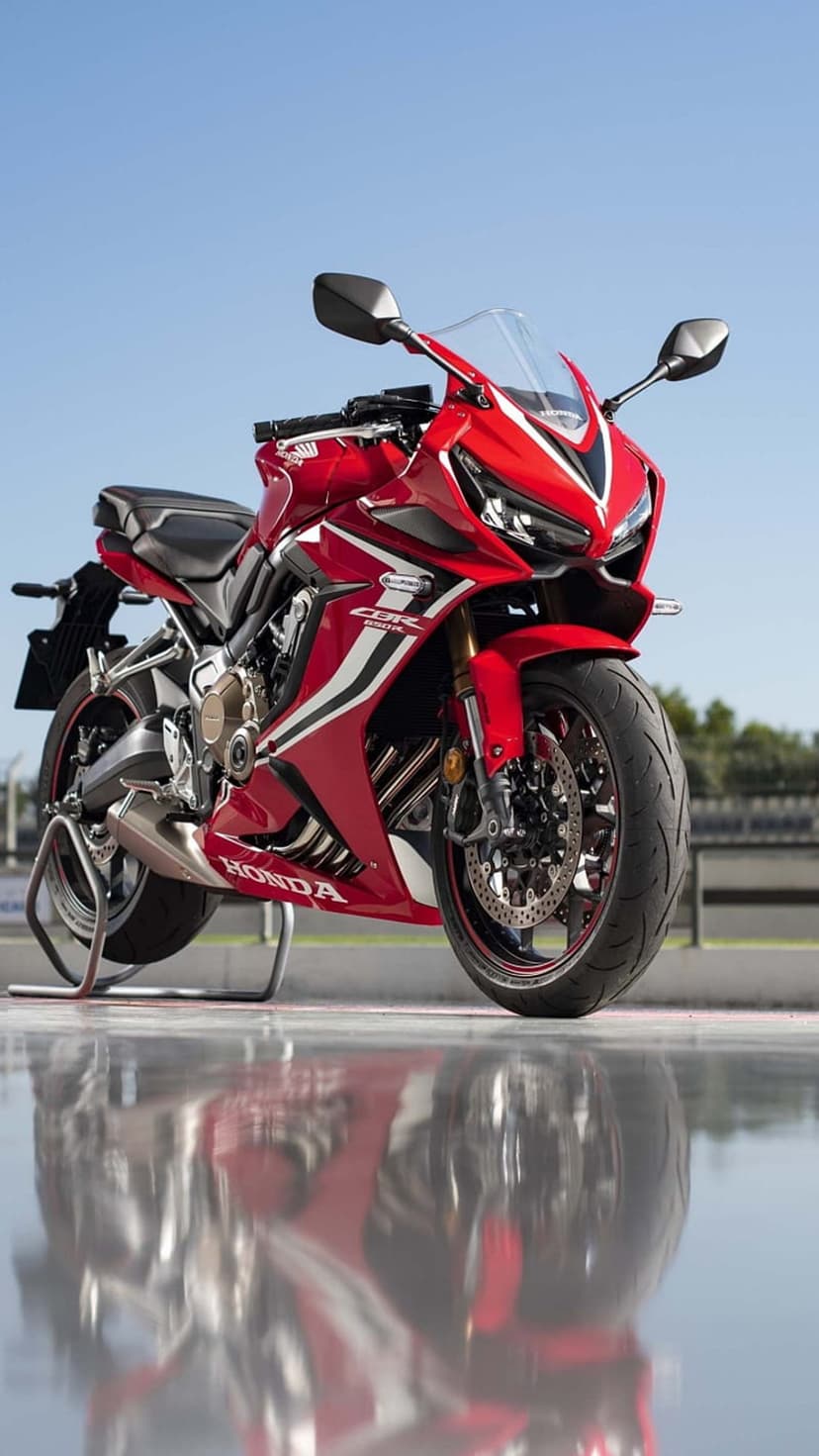 Red Honda CBR motorcycle reflecting on a wet racing track surface under a clear blue sky during the daytime.