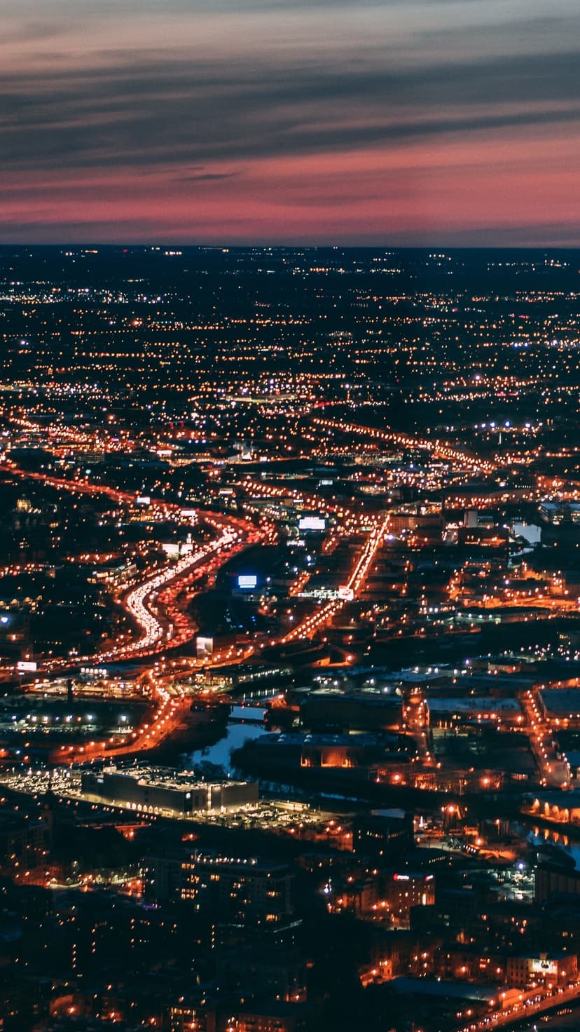 Glowing orange streetlights form a vast geometric grid across a dark city landscape seen from a high altitude.