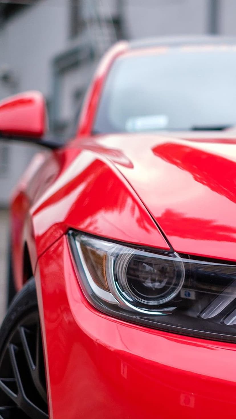 Ford Mustang headlight and red fender with glossy paint reflections and modern automotive styling details.