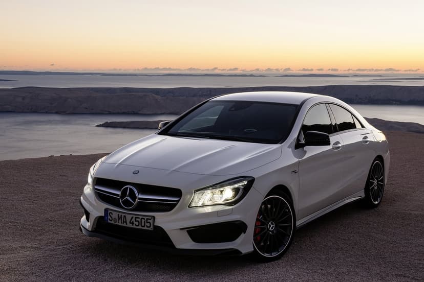 White Mercedes-Benz CLA 45 AMG on a cliff at sunset overlooking distant islands and a calm sea.