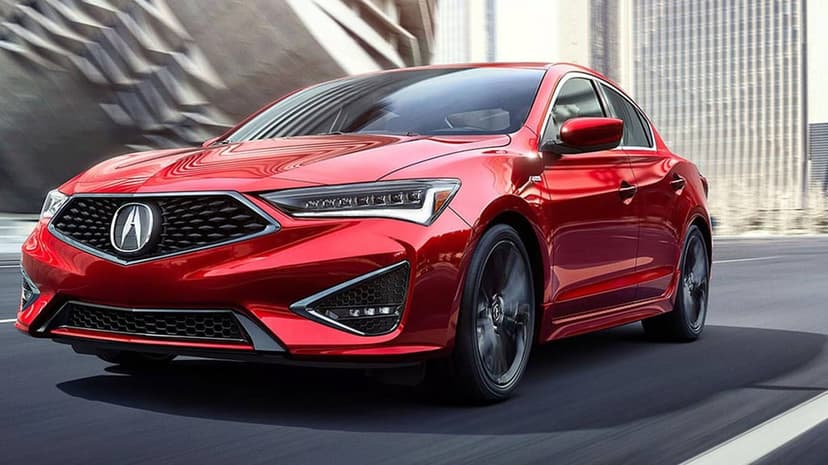 Red Acura ILX A-Spec sedan driving on a city street with motion-blurred wheels and urban background.