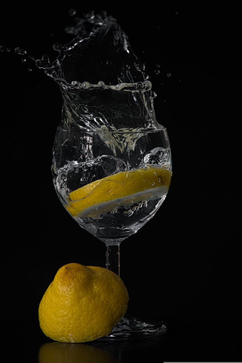 Lemon slice splashing into a water glass with dramatic spray droplets against a high-contrast dark background.