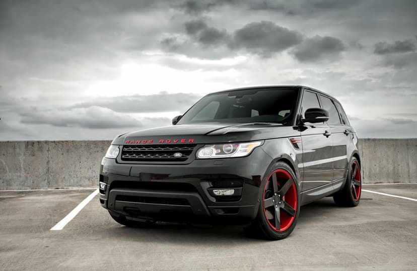 Black modified Range Rover Sport with red wheels on a concrete rooftop under a dramatic cloudy gray sky.
