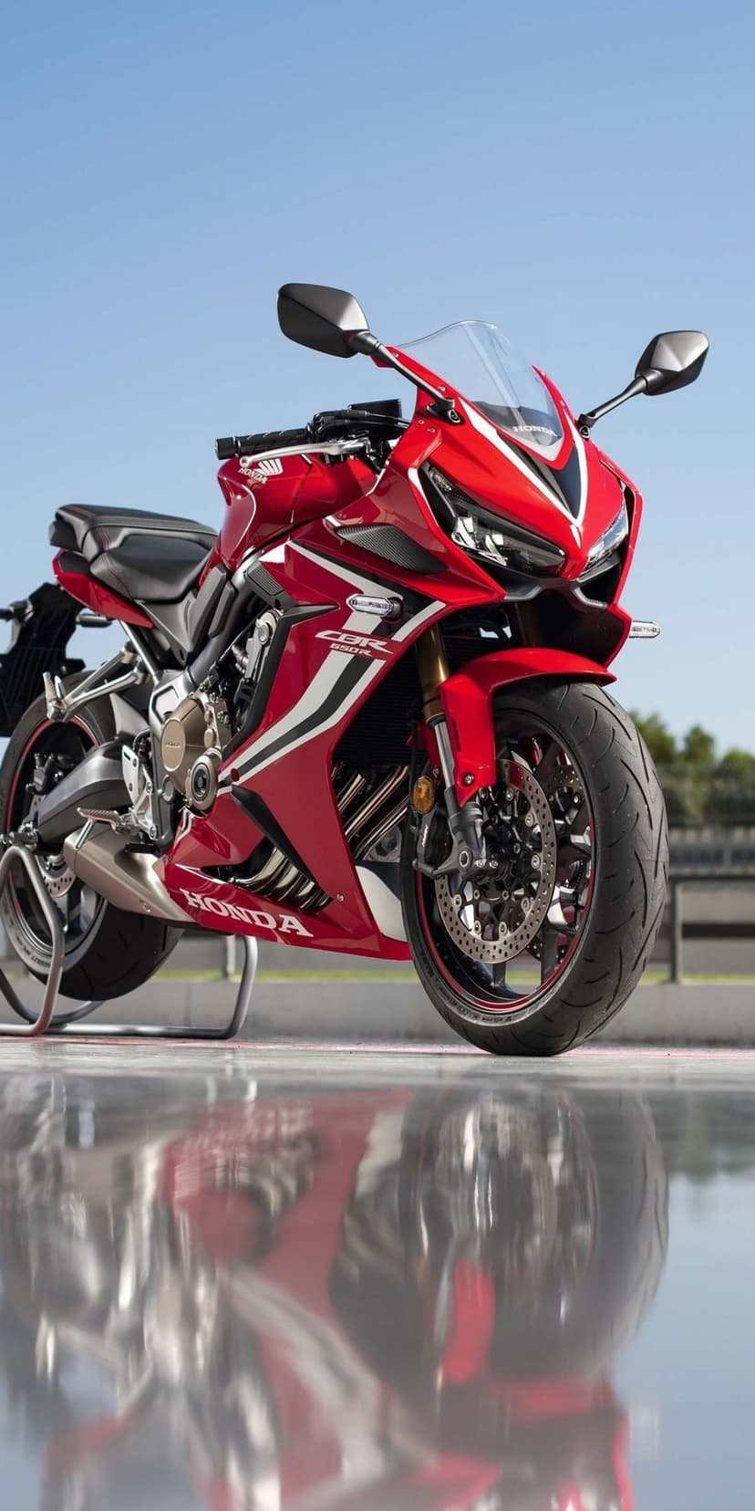 Red Honda CBR650R sportbike with white decals and gold forks parked on a reflective surface under a blue sky.