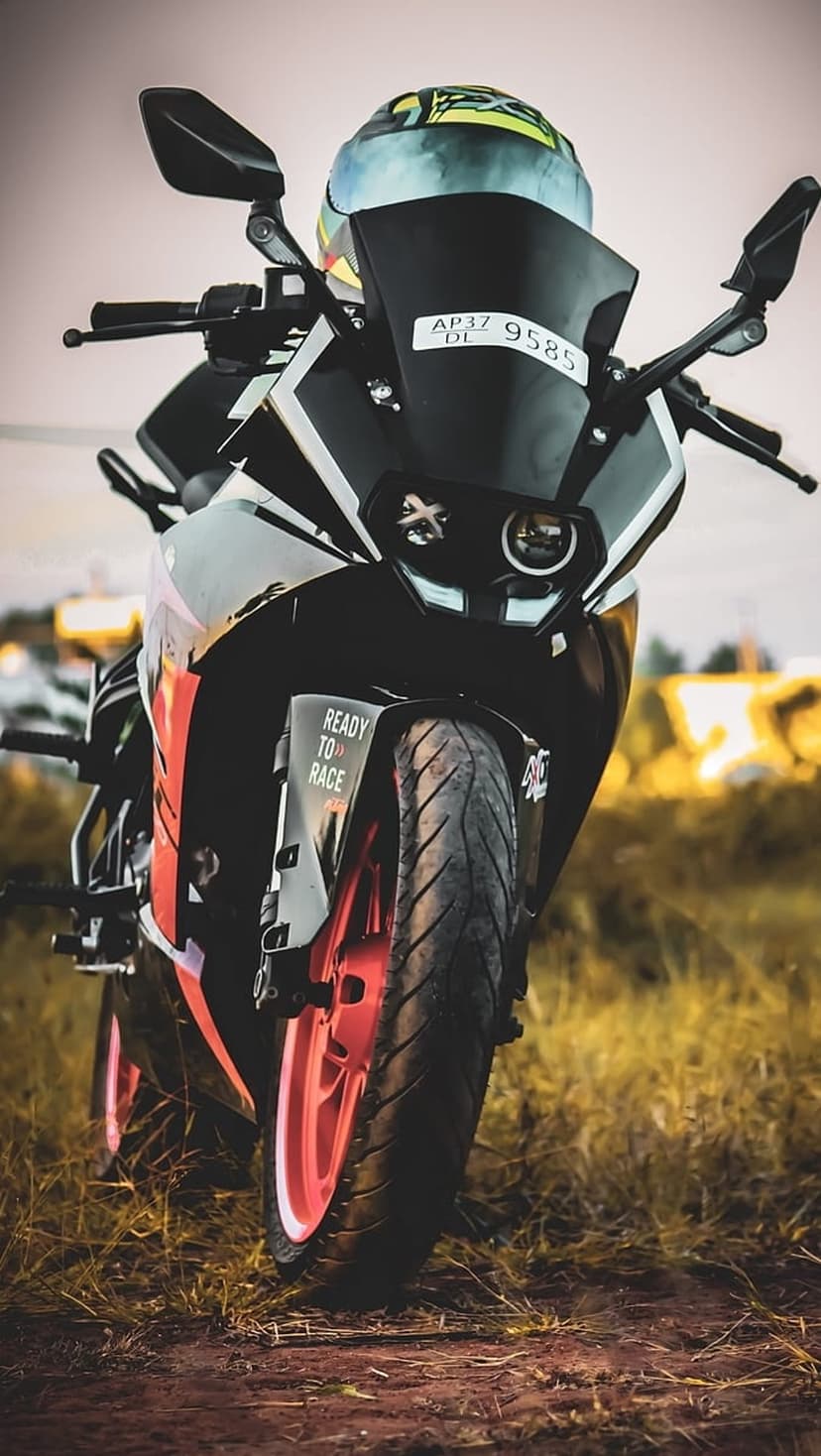 Orange and black sportbike with a colorful helmet on the seat parked on grass under soft natural lighting.