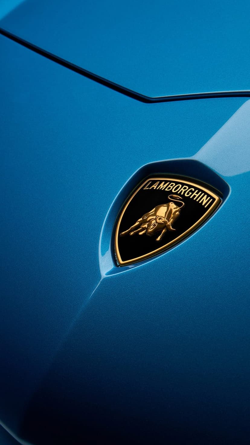 Gold Lamborghini crest with a raging bull emblem mounted on deep blue metallic car paint in sharp focus.