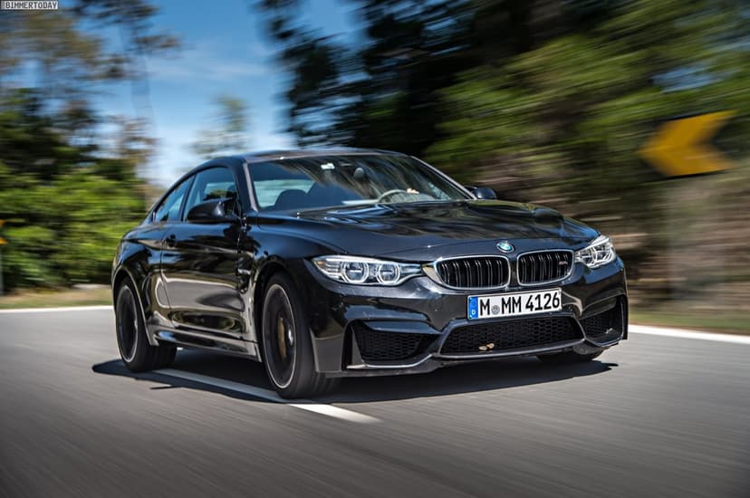 Black BMW M4 sports coupe driving fast on a sunlit road with heavy motion blur in the background.
