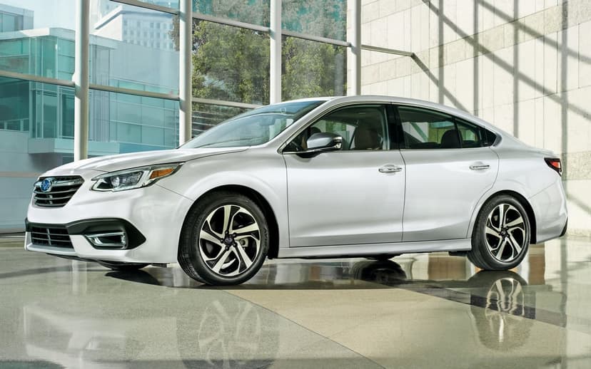Silver Subaru Legacy sedan parked in a sunlit glass lobby with leafy trees visible through the windows.