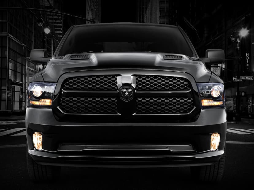Front view of a black Ram truck with glowing amber headlights parked on a dark city street at night.
