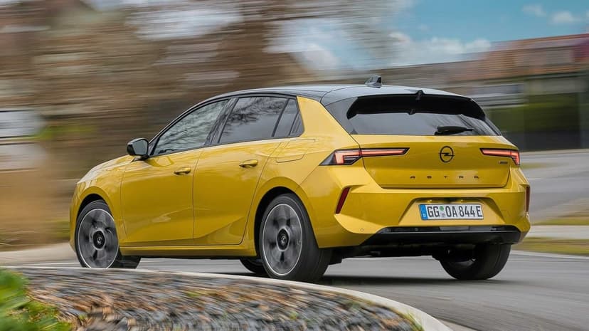 Yellow Opel Astra driving on a road with motion blur, showing the rear LED lights and black roof.