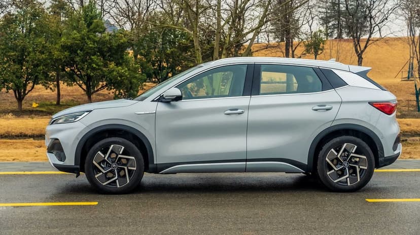 Side view of a silver electric SUV parked on a wet road with yellow lines against a park background.