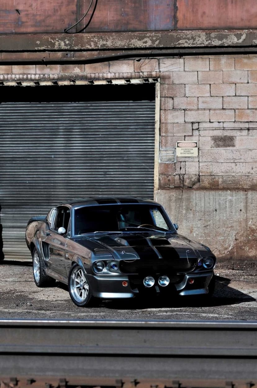 Metallic grey custom Mustang with black stripes parked in front of a brick industrial building.