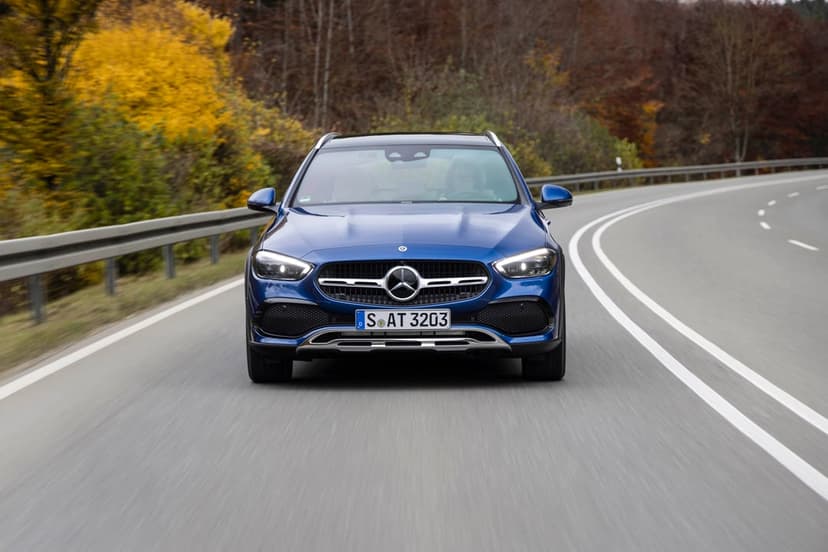 Front view of a blue Mercedes-Benz driving on a winding road through a forest with yellow autumn leaves.