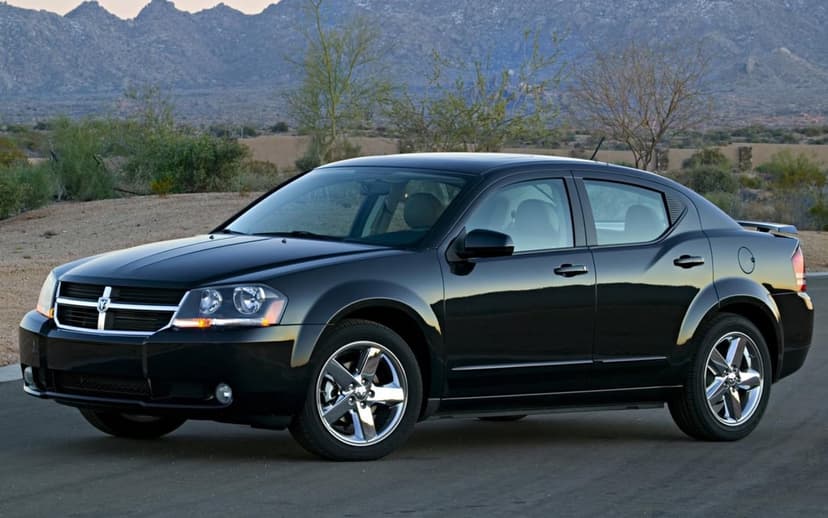 Black Dodge Avenger sedan with chrome wheels parked in a desert landscape with mountains in the background.