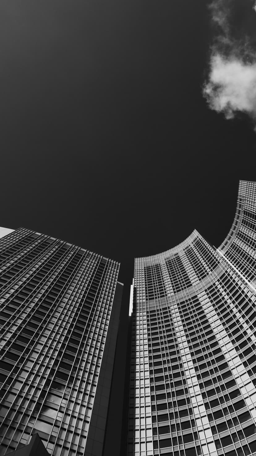 Modern skyscrapers soar toward a dark sky with clouds in a high-contrast black and white low-angle perspective.