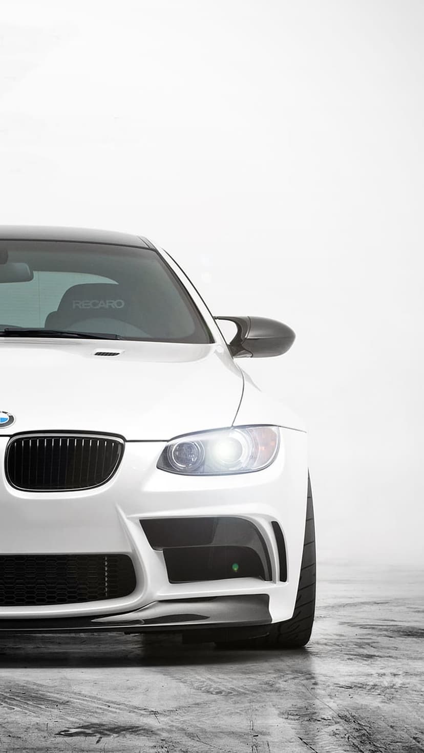 White BMW M3 coupe with LED headlights, carbon fiber splitter, and Recaro racing seats in a bright studio space.