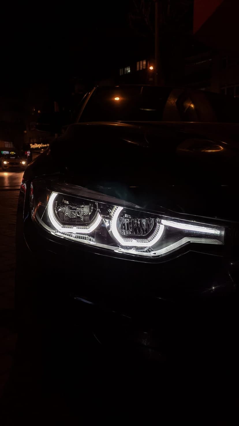 LED car headlight with glowing halo rings and sharp daytime running lights against a dark night background.