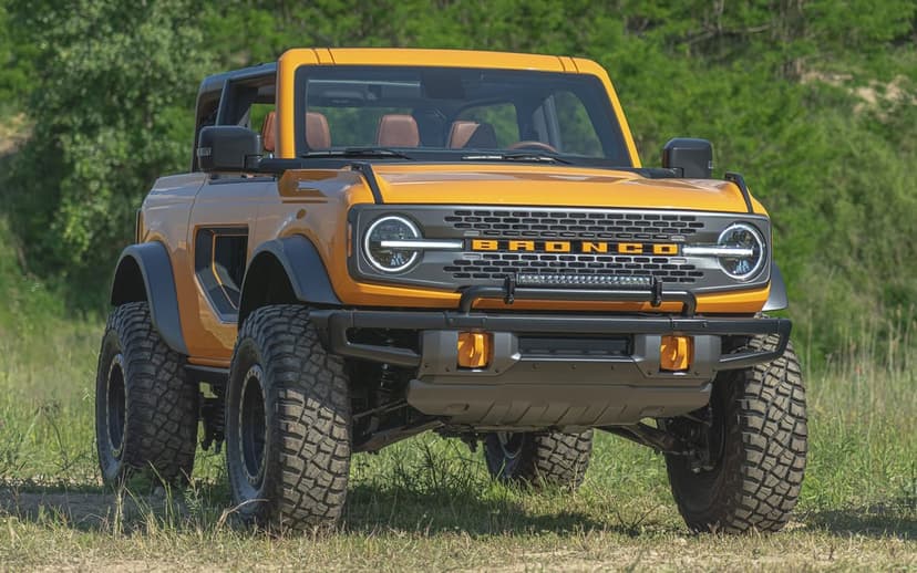 Orange Ford Bronco off-roader with oversized tires and light bar parked in a sunny green field.
