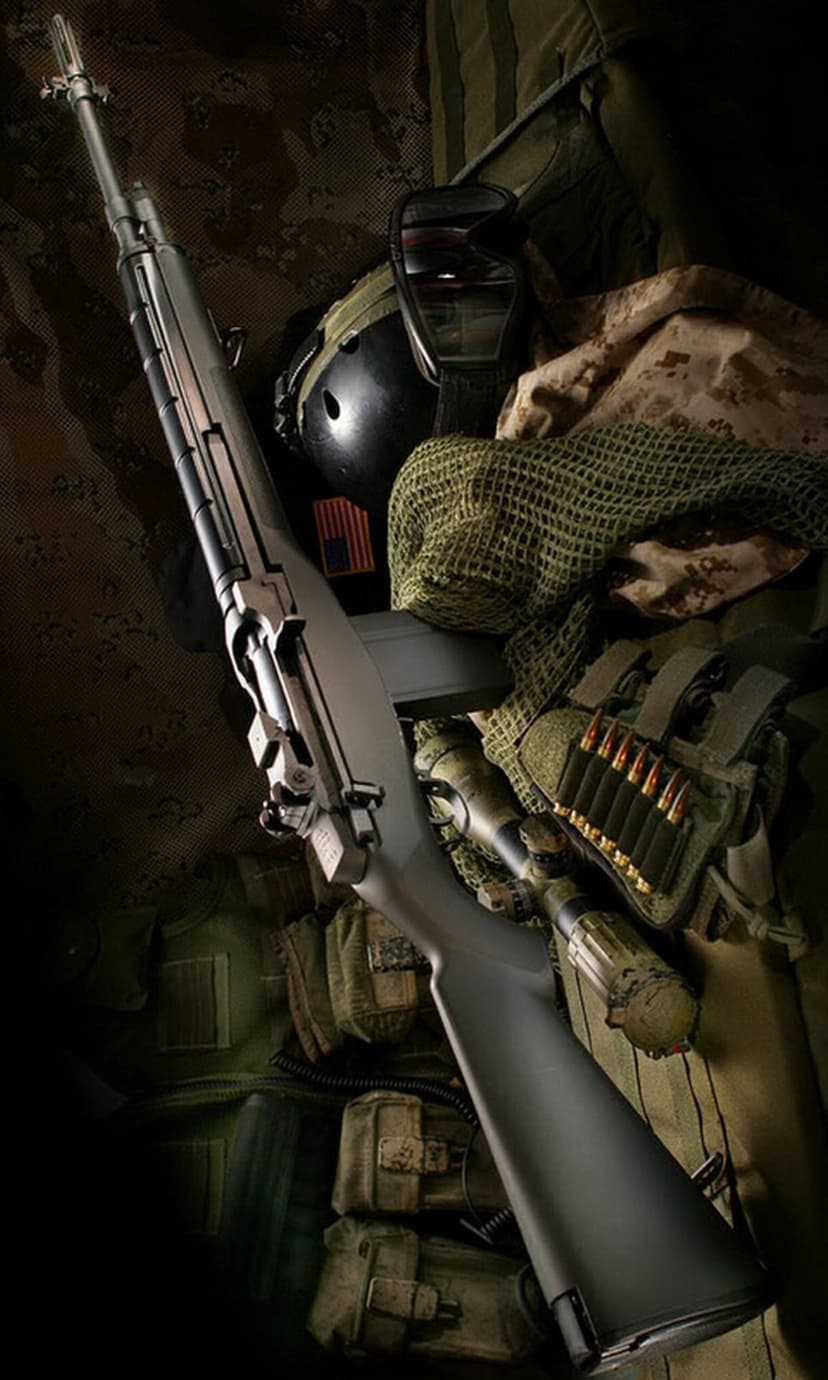 Assault rifle and ballistic helmet with an American flag patch sit against a dark textured background.
