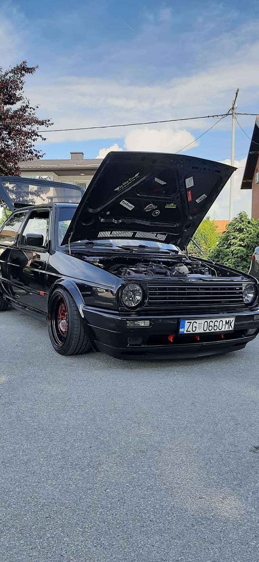 Black Volkswagen Golf Mk2 with a raised hood revealing a custom engine bay parked on asphalt under a blue sky.