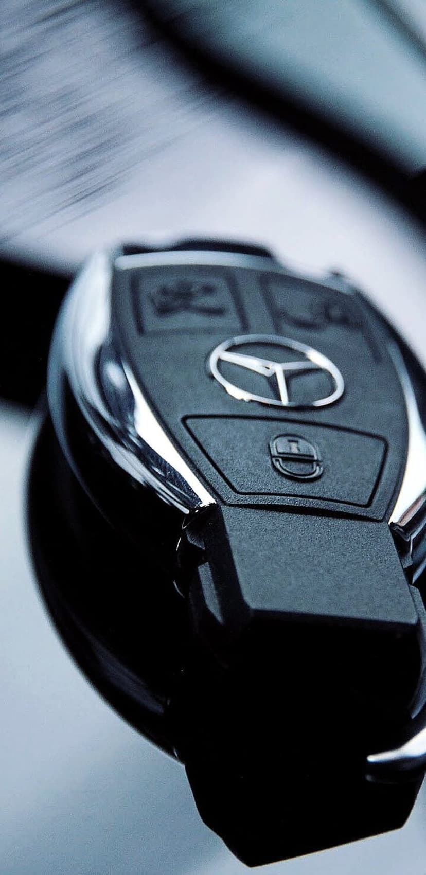 Mercedes-Benz car key fob featuring a silver logo, textured black surface, and chrome buttons on a blurred backdrop.