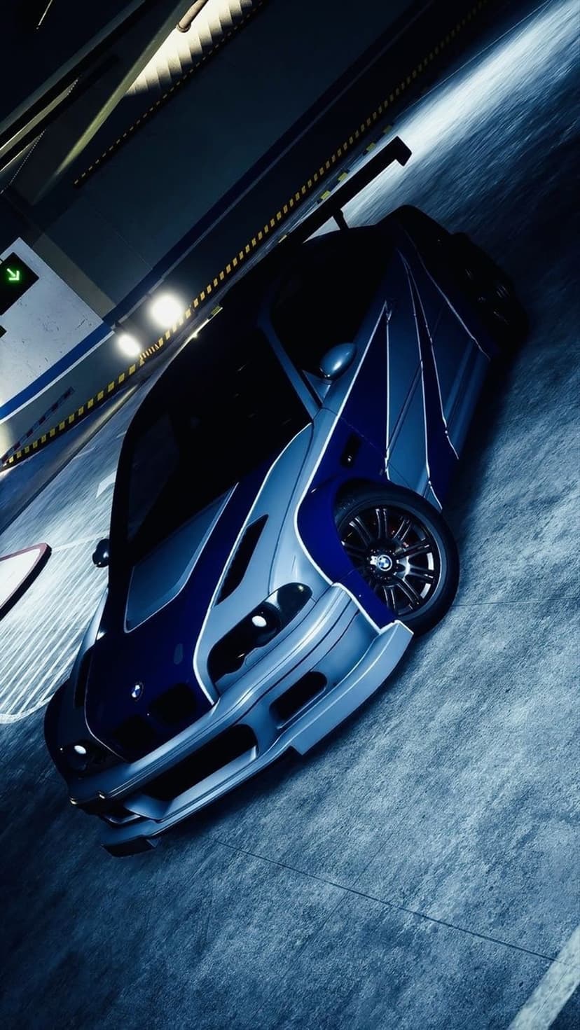 Blue sports car with silver racing stripes and a rear spoiler parked in a shadowy concrete parking garage.
