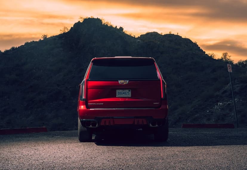 Red Cadillac Escalade V rear view parked at a mountain overlook during a vibrant orange and gold desert sunset.