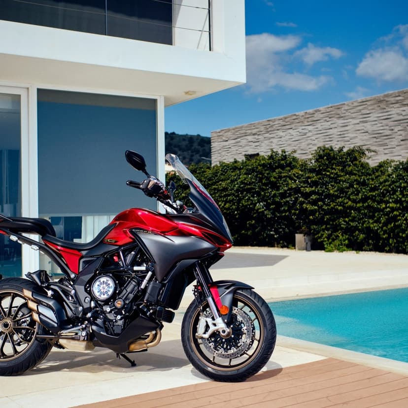 Red and black sport touring motorcycle parked by a clear blue swimming pool outside a modern white villa.