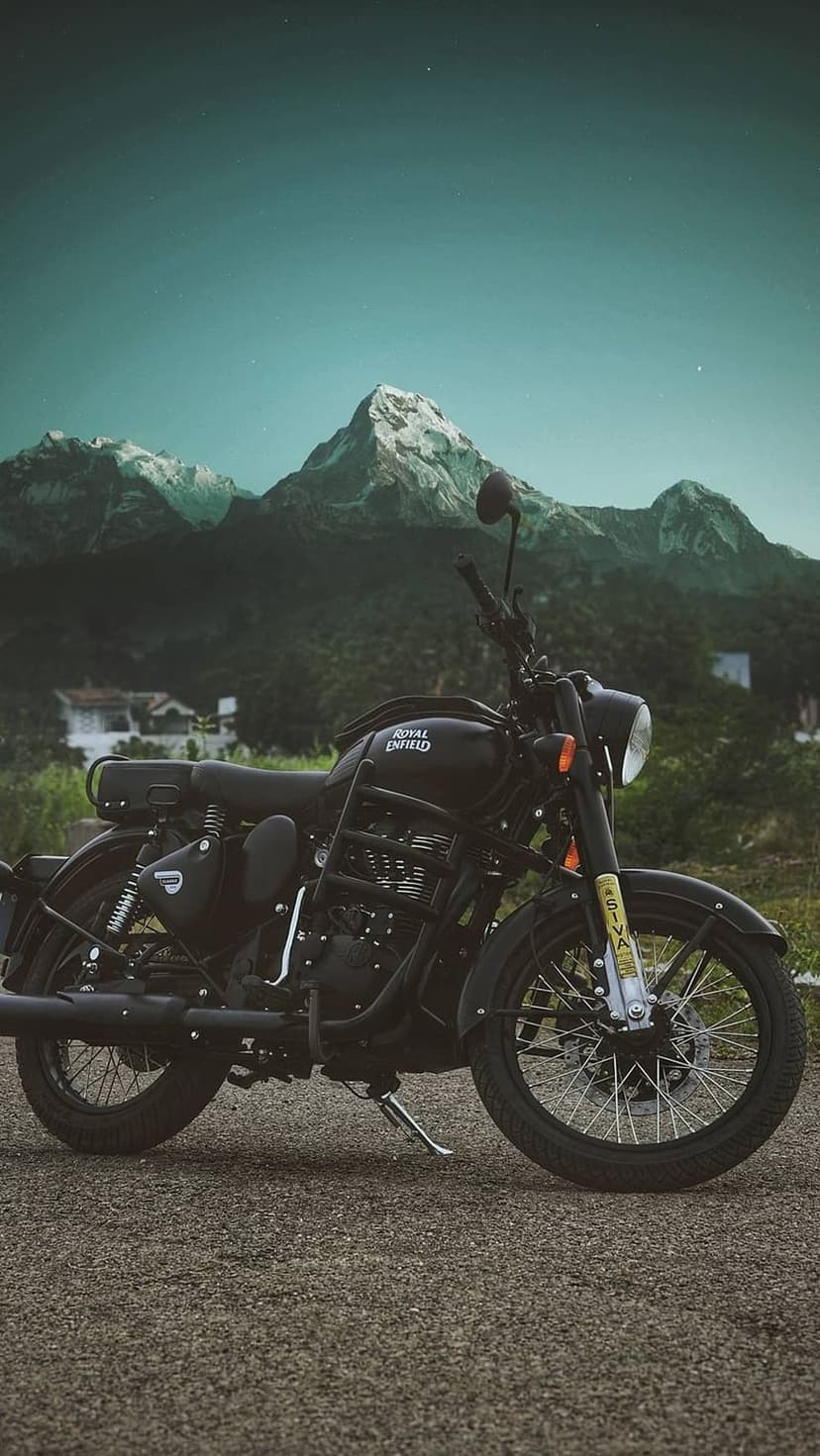 Royal Enfield motorcycle parked on a gravel road facing snow-covered mountains under a purple twilight sky.