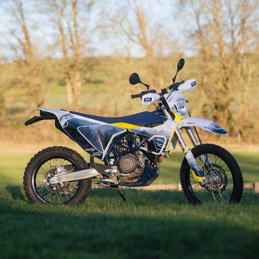 Husqvarna 701 Enduro motorcycle with mountain graphics parked in a field with golden hour lighting.
