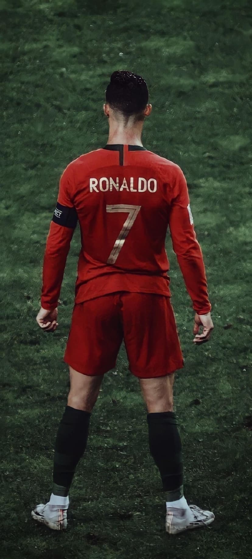 Cristiano Ronaldo seen from behind wearing a red Portugal jersey with number seven on a green football field.