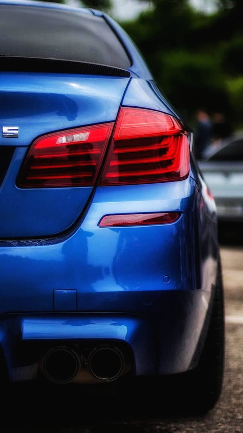 BMW M5 rear bumper featuring glowing red LED taillights, quad exhaust tips, and metallic blue paintwork.