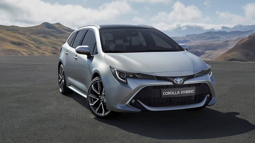 Silver Toyota Corolla Hybrid on a mountain road overlooking a scenic valley under a bright blue sky.