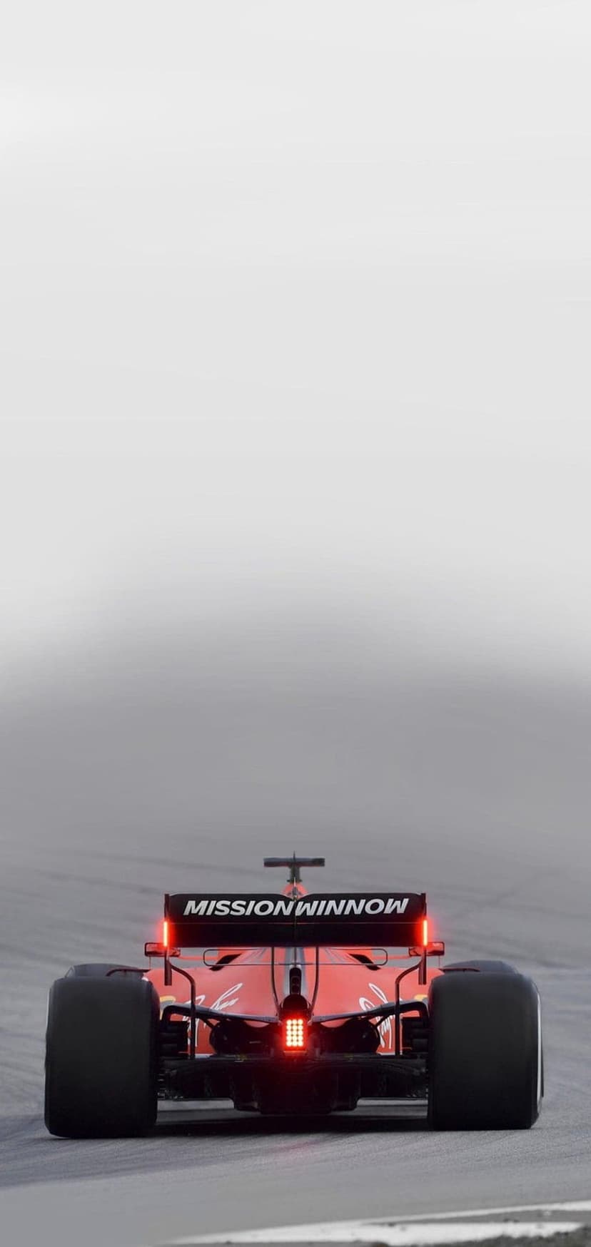 Ferrari F1 car rear wing with glowing red brake lights and Mission Winnow logo on a blurred racetrack background.