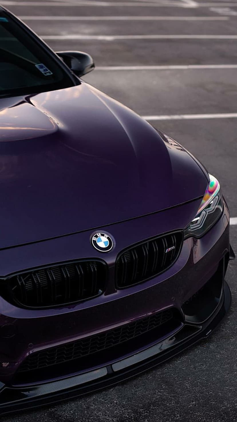 Purple BMW M4 front view featuring a black kidney grille, sharp LED headlights, and a blurred asphalt background.