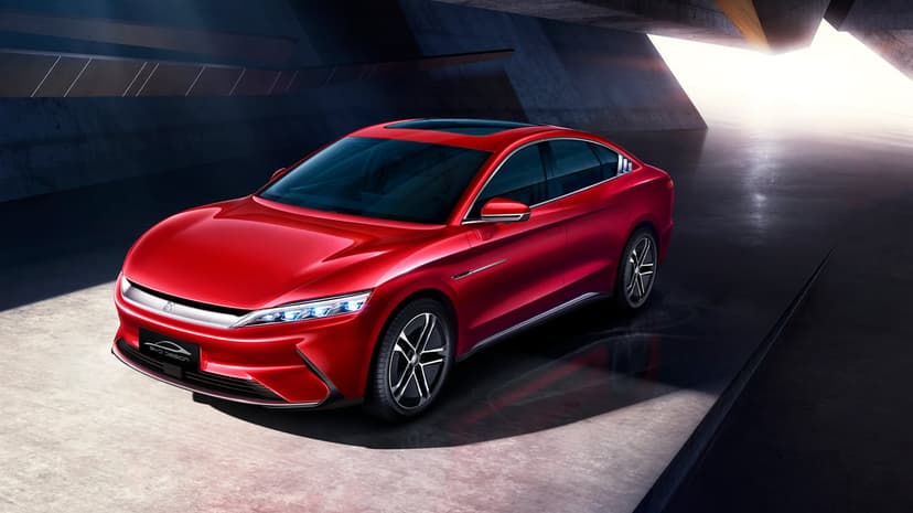 Sleek red electric sedan parked in a minimalist concrete architectural space with dramatic lighting.