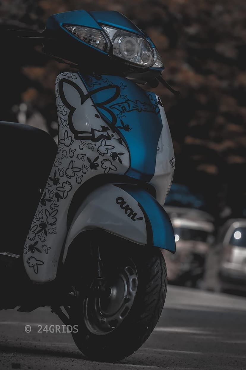 Blue and white scooter with Playboy bunny decals and OUCH text parked on a blurred urban street background.